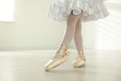 Photo of Little ballerina practicing dance moves indoors, closeup. Space for text