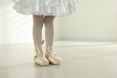 Little ballerina wearing pointe shoes indoors, closeup. Space for text