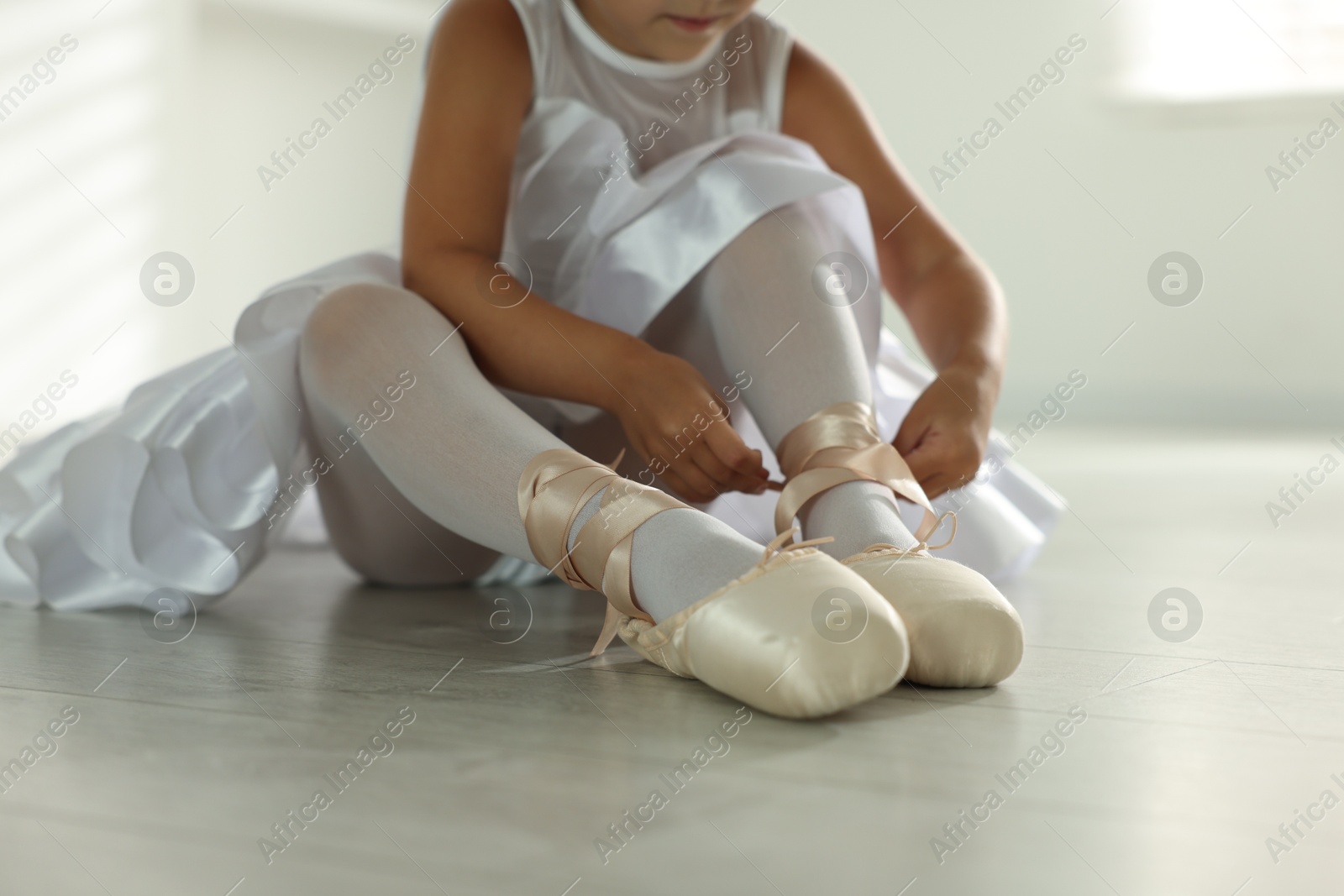 Photo of Little ballerina tying pointe shoes indoors, closeup