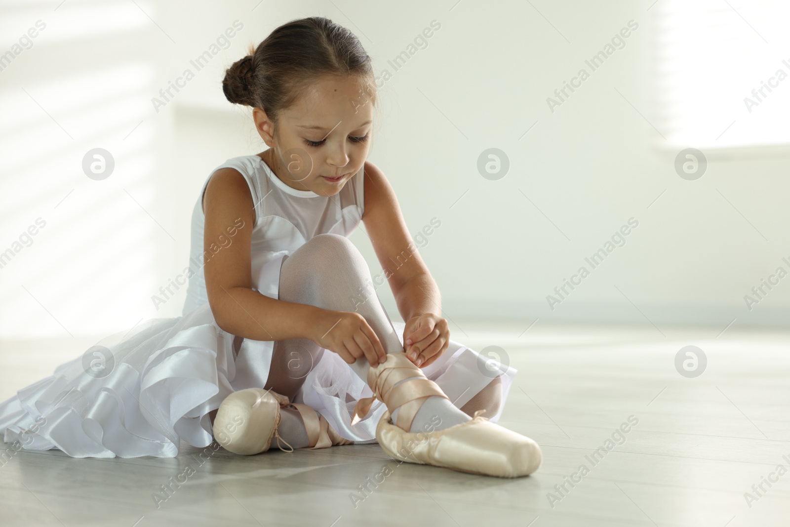 Photo of Little ballerina tying pointe shoes indoors, space for text