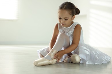 Photo of Little ballerina tying pointe shoes indoors, space for text