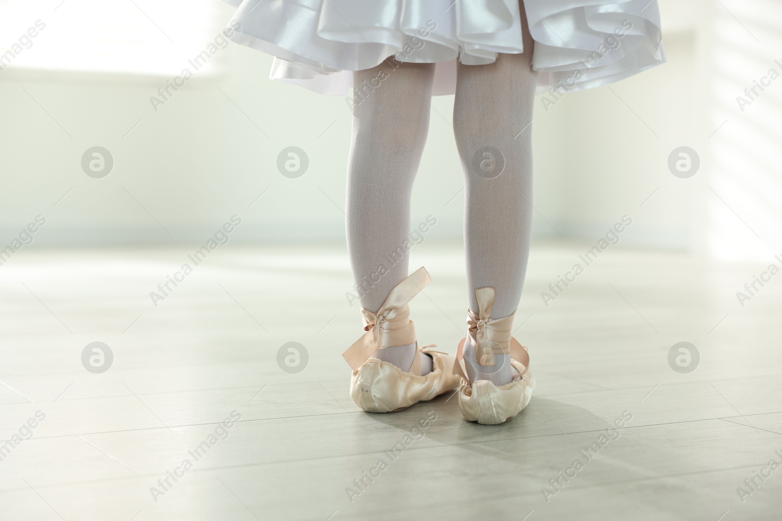 Photo of Little ballerina wearing pointe shoes indoors, closeup