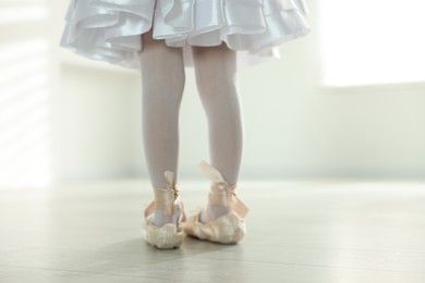 Little ballerina wearing pointe shoes indoors, closeup