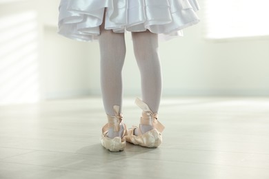 Photo of Little ballerina wearing pointe shoes indoors, closeup