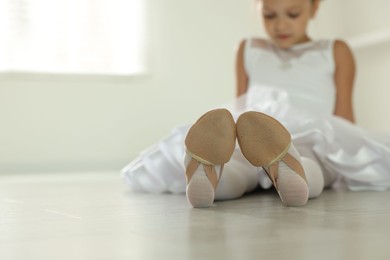 Little ballerina wearing pointe shoes indoors, selective focus. Space for text