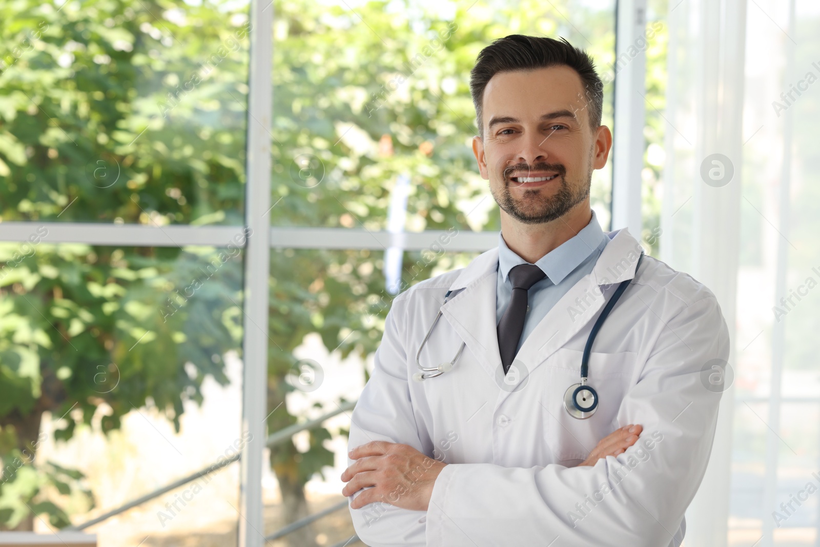 Photo of Smiling doctor with stethoscope indoors, space for text