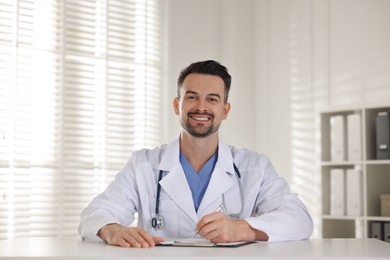 Smiling doctor with clipboard at table in clinic