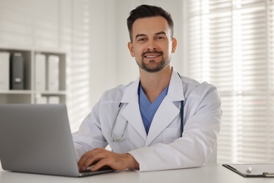 Photo of Smiling doctor working with laptop at table in clinic