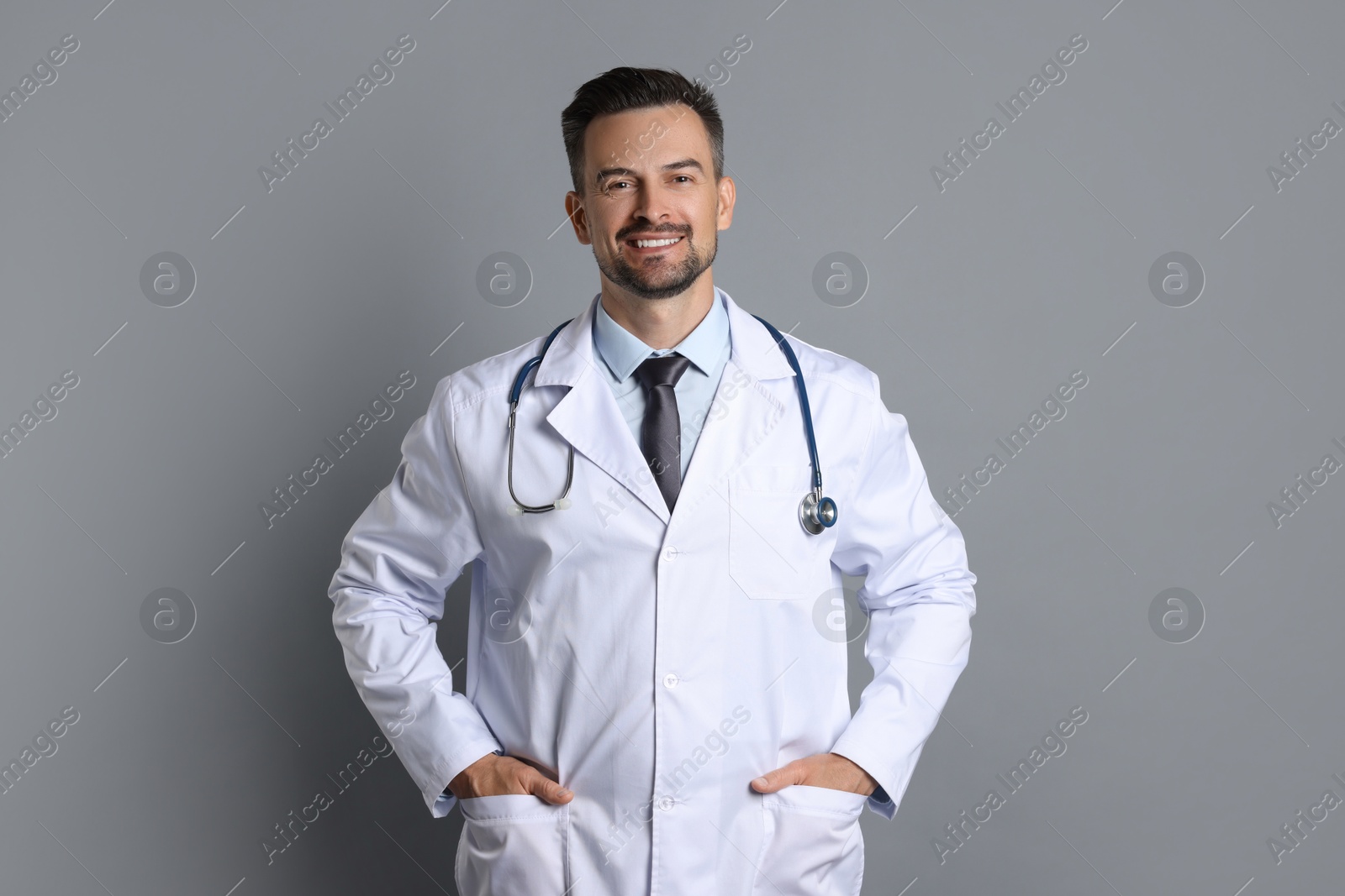 Photo of Smiling doctor with stethoscope on grey background