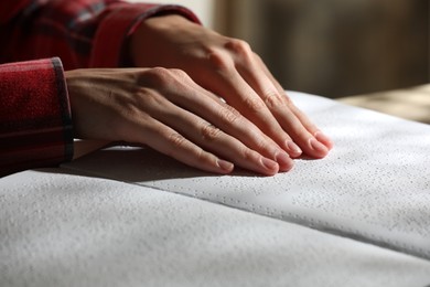 Photo of Blind woman reading book written in Braille at table, closeup