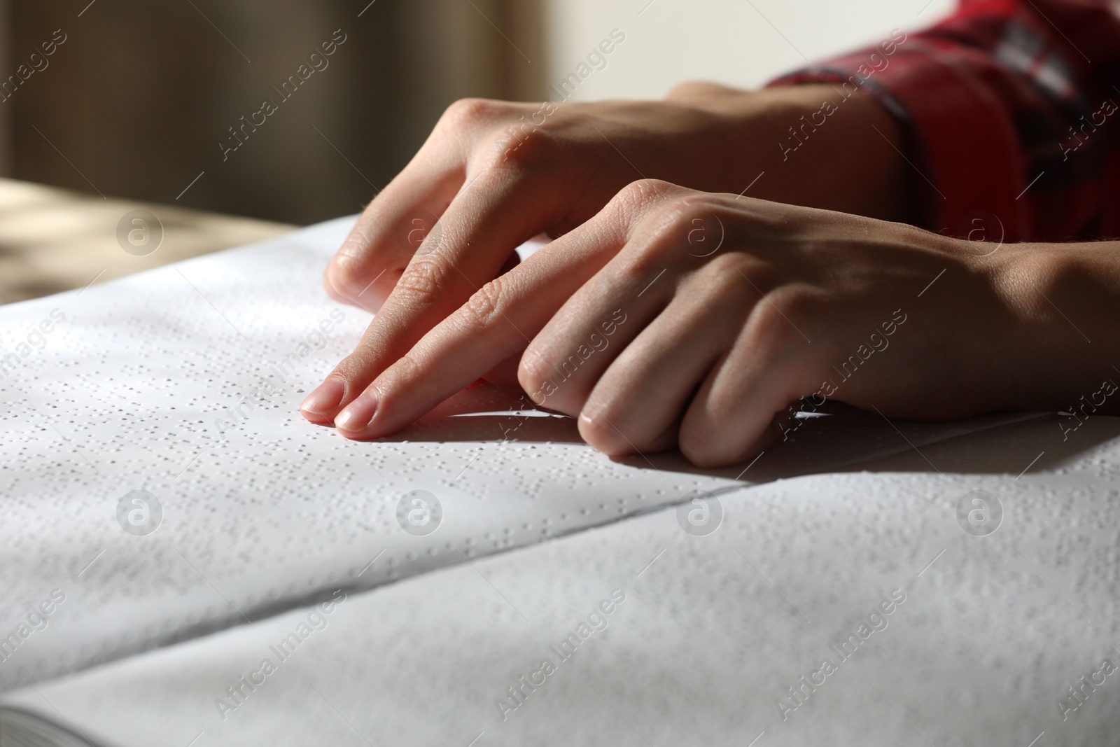 Photo of Blind woman reading book written in Braille at table, closeup