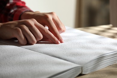 Photo of Blind woman reading book written in Braille at table, closeup