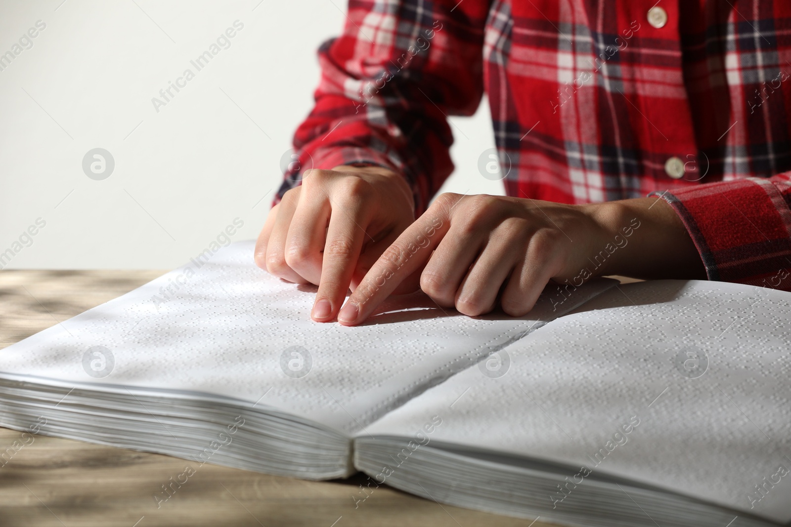 Photo of Blind woman reading book written in Braille at table, closeup