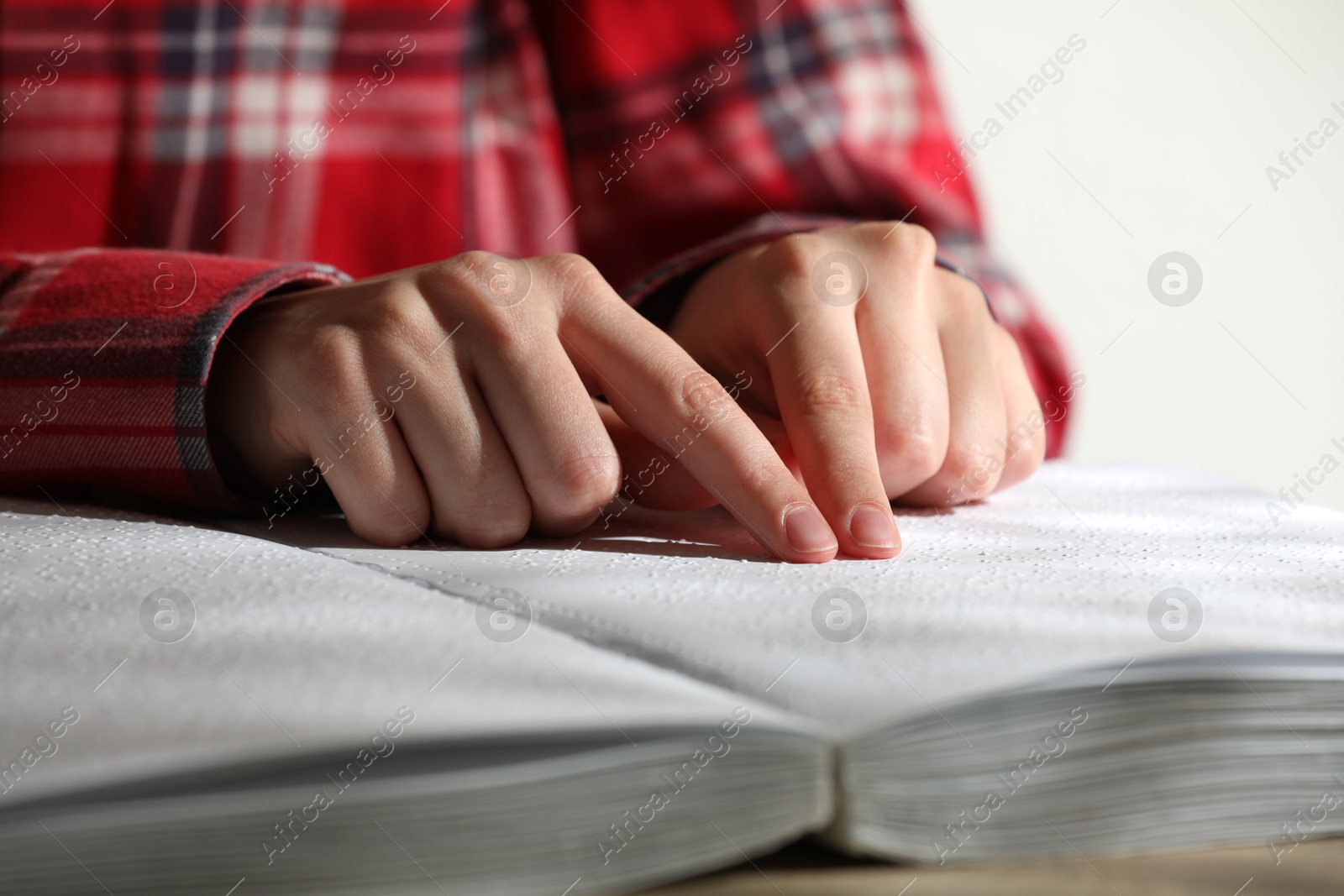 Photo of Blind woman reading book written in Braille at table, closeup