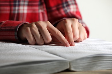 Photo of Blind woman reading book written in Braille at table, closeup