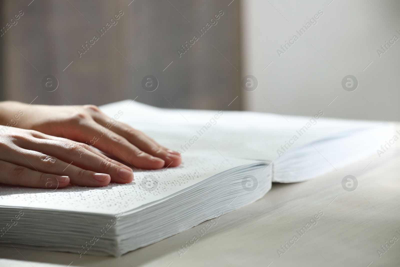 Photo of Blind woman reading book written in Braille at wooden table, closeup