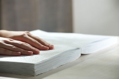 Blind woman reading book written in Braille at wooden table, closeup