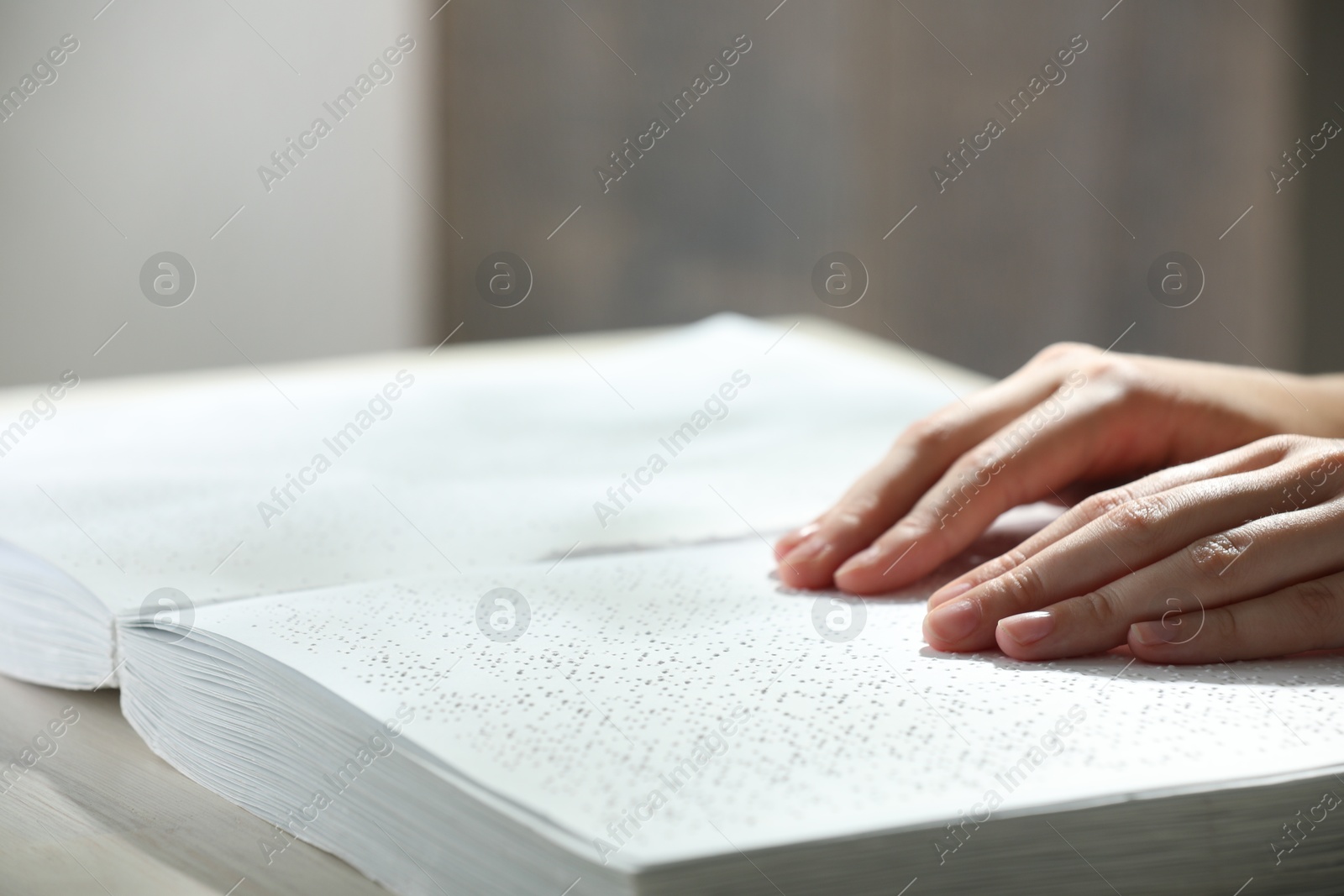 Photo of Blind woman reading book written in Braille at wooden table, closeup