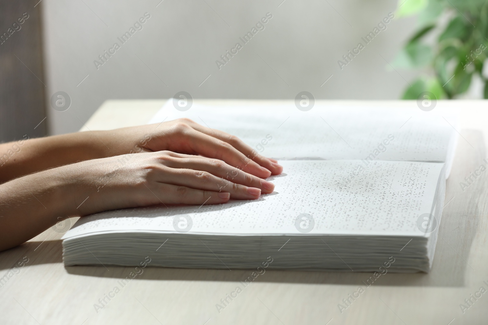 Photo of Blind woman reading book written in Braille at wooden table, closeup