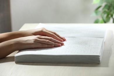 Blind woman reading book written in Braille at wooden table, closeup