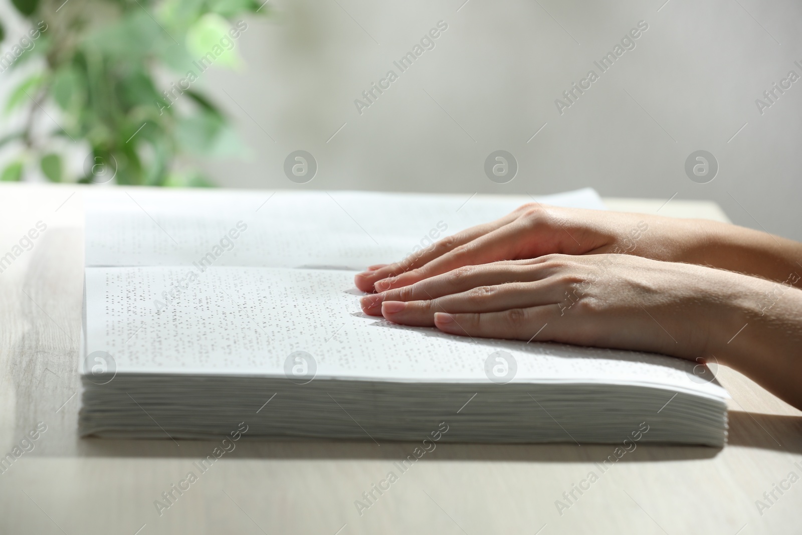 Photo of Blind woman reading book written in Braille at wooden table, closeup