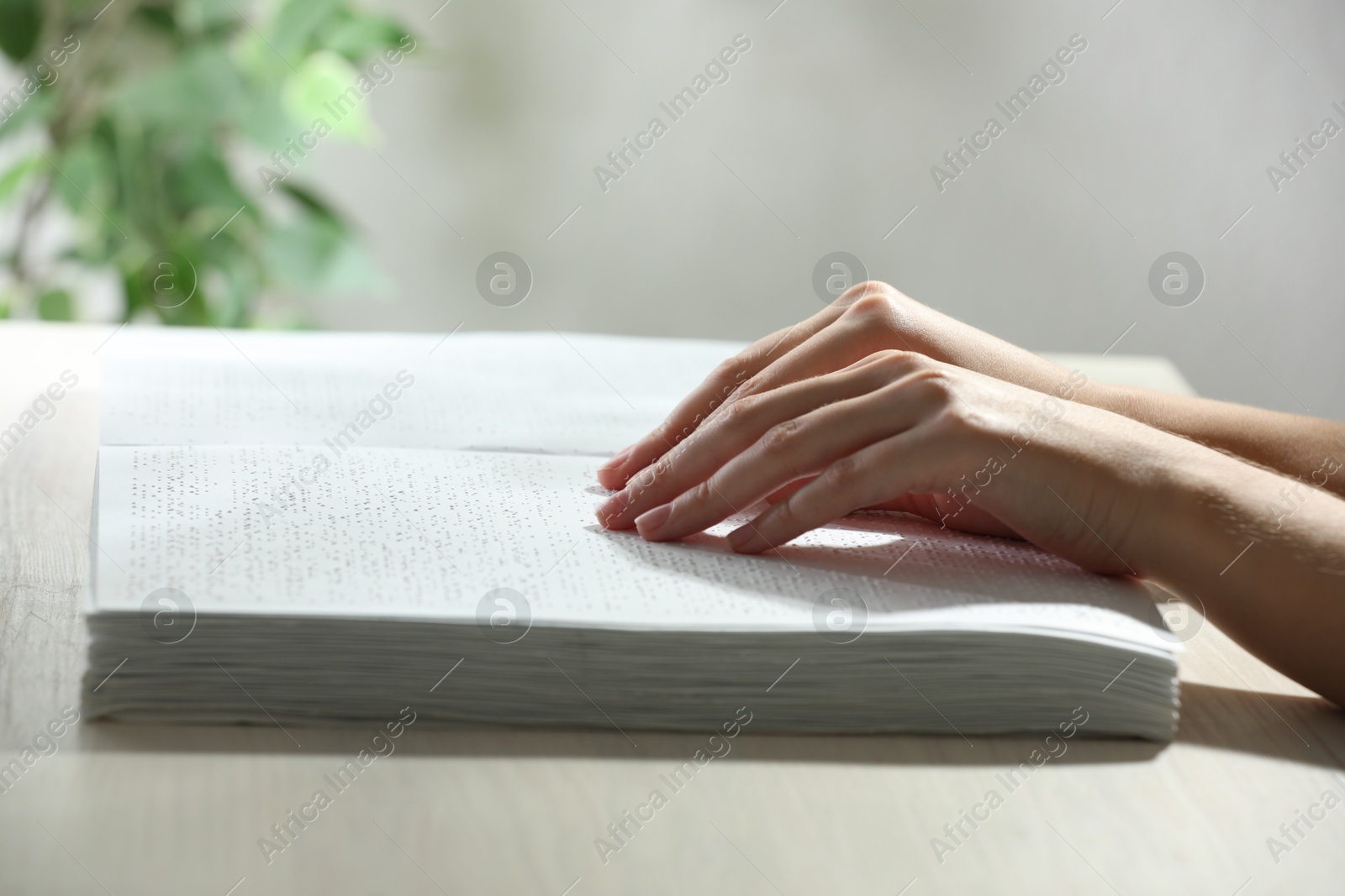 Photo of Blind woman reading book written in Braille at wooden table, closeup