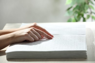 Photo of Blind woman reading book written in Braille at wooden table, closeup