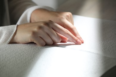 Photo of Blind woman reading book written in Braille at table, closeup