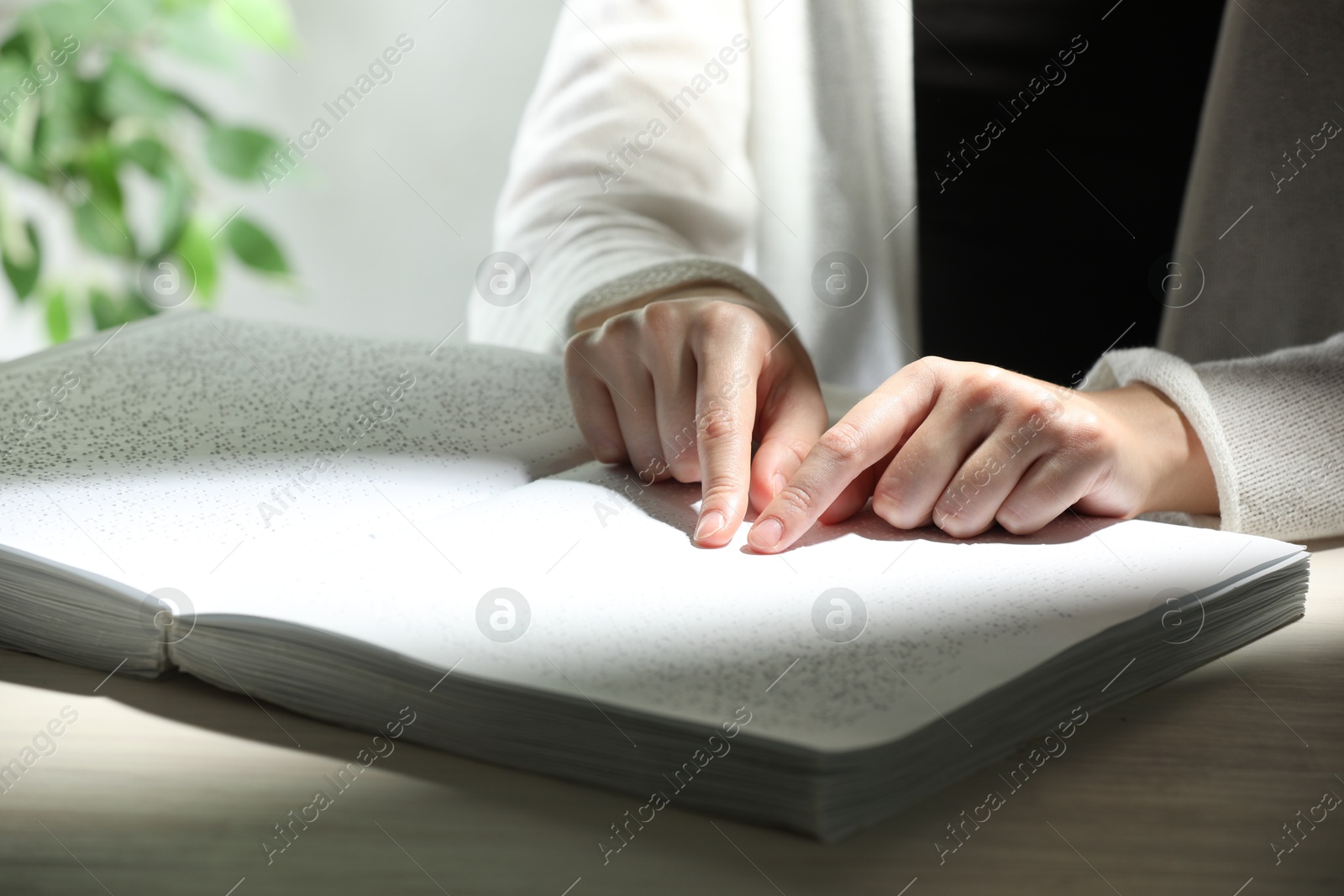 Photo of Blind woman reading book written in Braille at wooden table, closeup