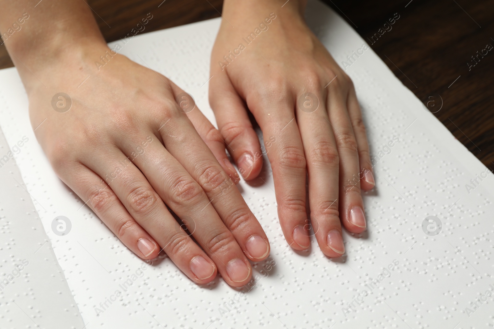 Photo of Blind woman reading book written in Braille at wooden table, closeup