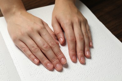 Photo of Blind woman reading book written in Braille at wooden table, closeup