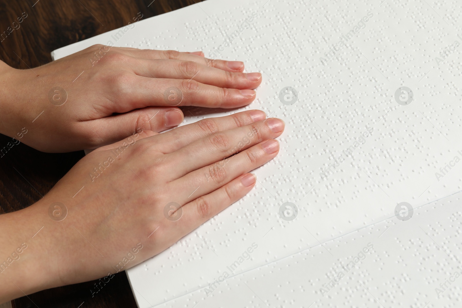 Photo of Blind woman reading book written in Braille at wooden table, closeup