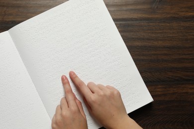 Photo of Blind woman reading book written in Braille at wooden table, top view