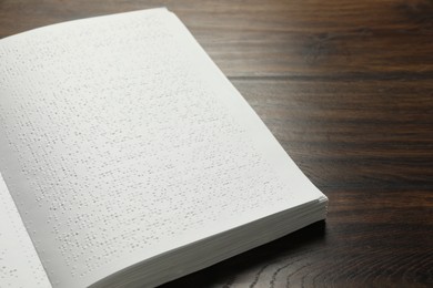 Photo of Book with Braille text on wooden table, closeup. Education and leisure for blind people