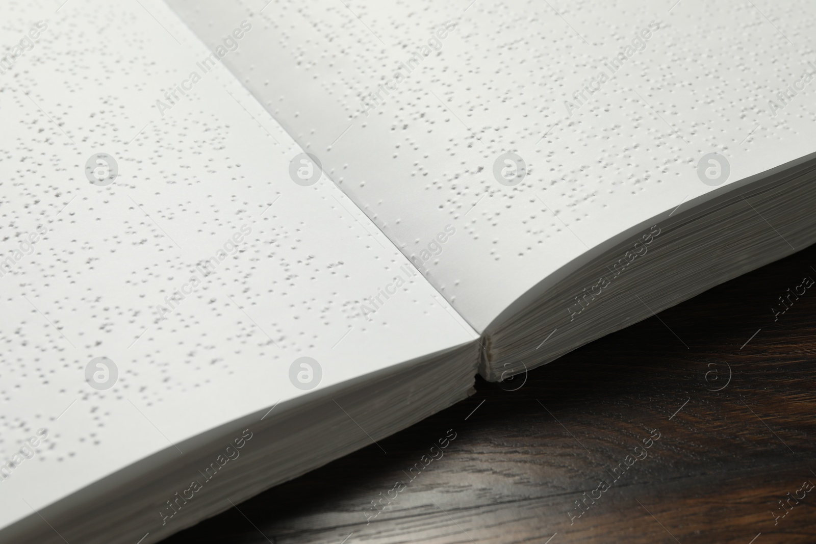 Photo of Book with Braille text on wooden table, closeup. Education and leisure for blind people