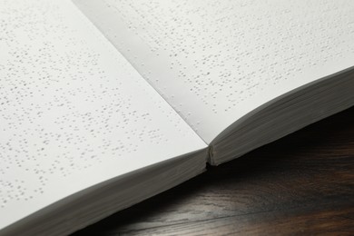 Photo of Book with Braille text on wooden table, closeup. Education and leisure for blind people