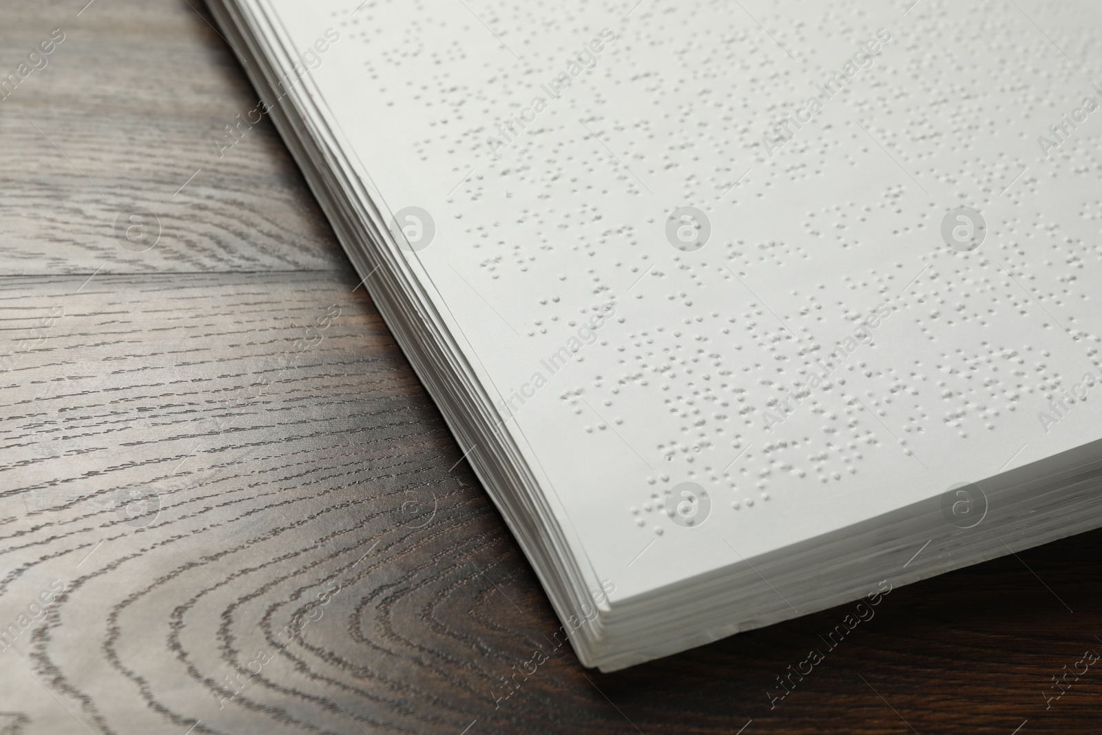 Photo of Book with Braille text on wooden table, closeup. Education and leisure for blind people