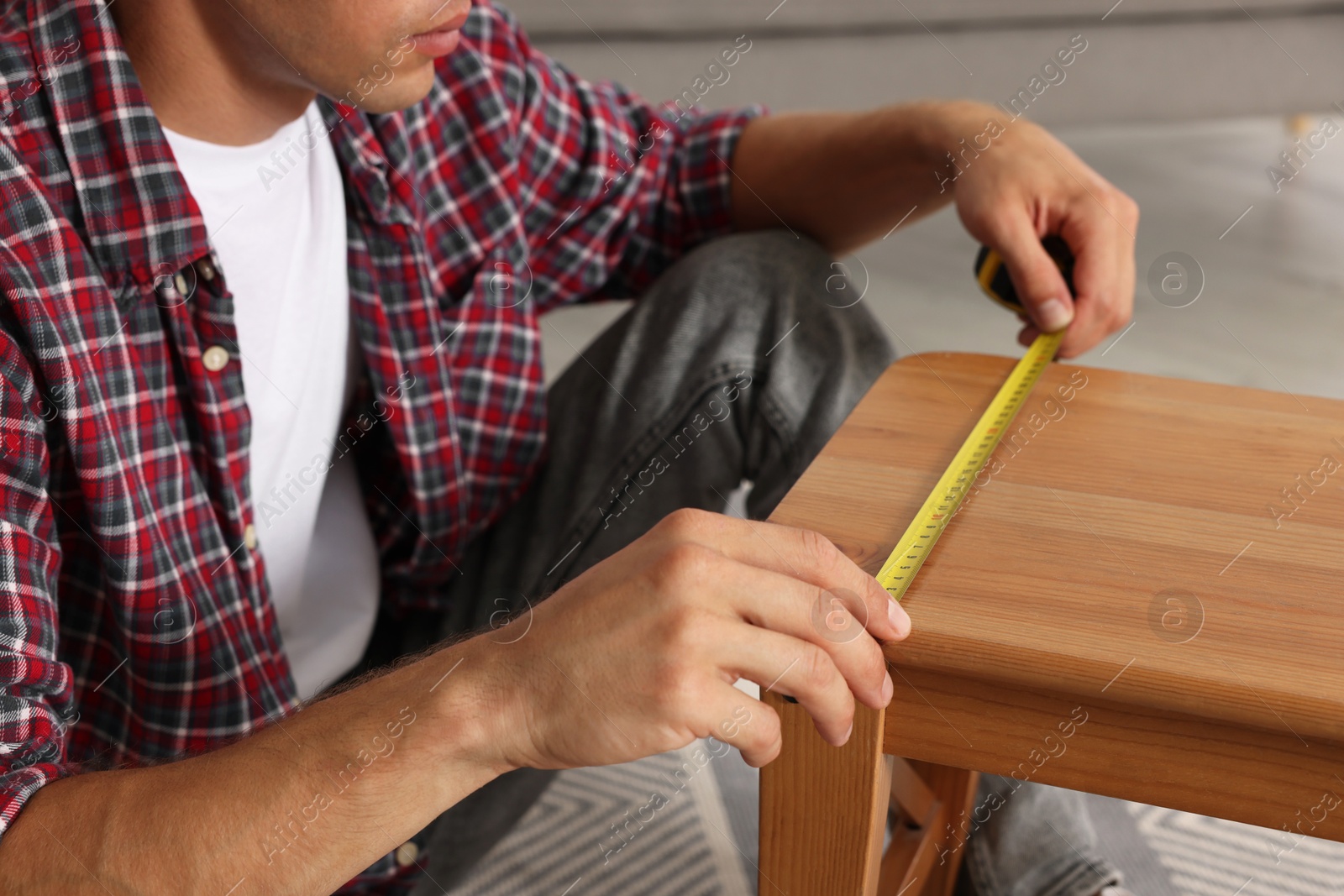 Photo of Man using tape measure while repairing wooden stool indoors, closeup