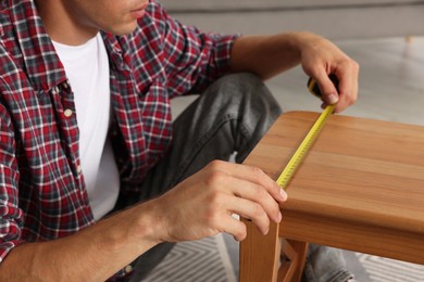 Man using tape measure while repairing wooden stool indoors, closeup