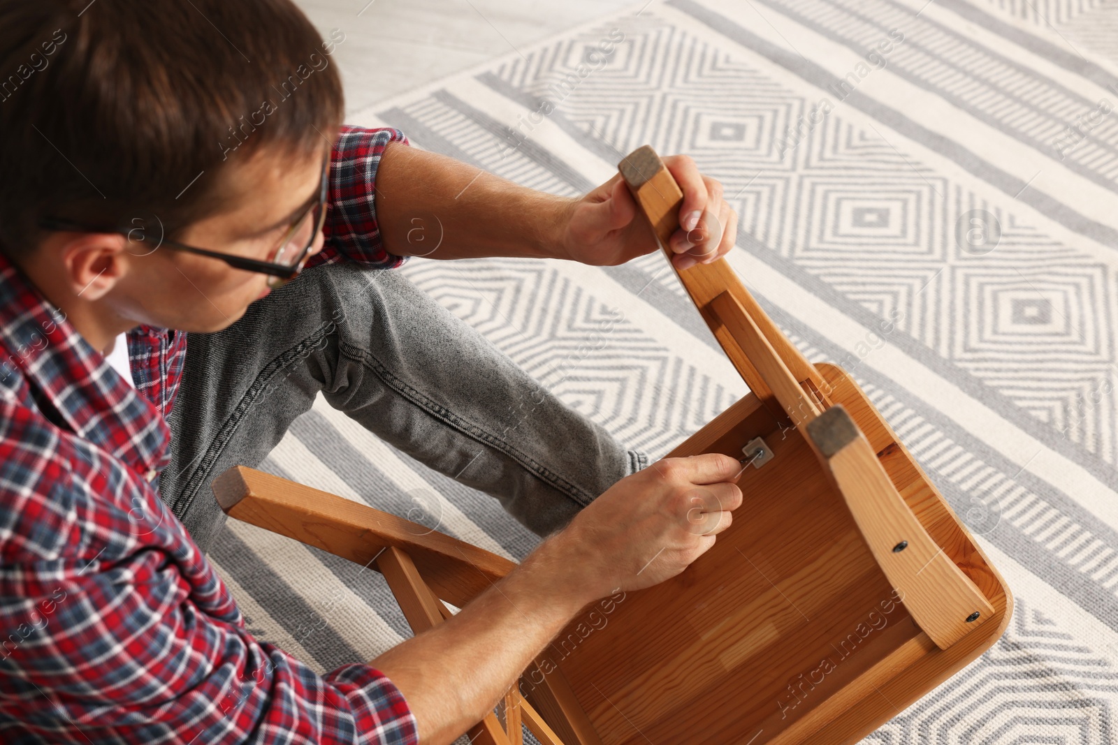 Photo of Man repairing wooden stool with screwdriver indoors