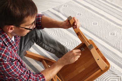 Man repairing wooden stool with screwdriver indoors