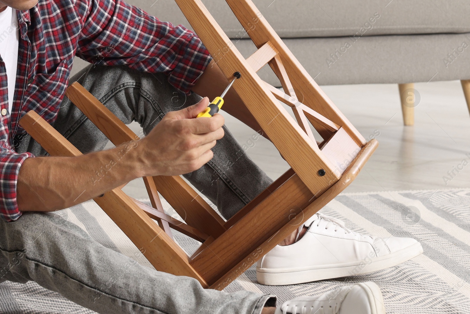 Photo of Man repairing wooden stool with screwdriver indoors, closeup