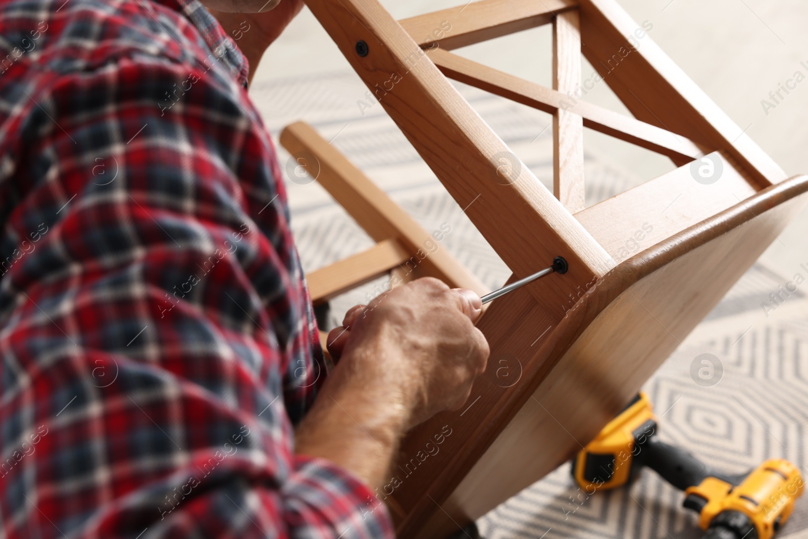 Photo of Man repairing wooden stool with screwdriver indoors, closeup