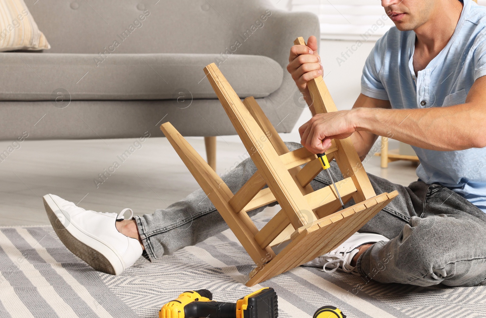 Photo of Man repairing wooden stool with screwdriver indoors, closeup