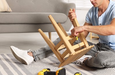 Photo of Man repairing wooden stool with screwdriver indoors, closeup