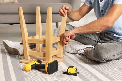 Photo of Man repairing wooden stool with screwdriver indoors, closeup