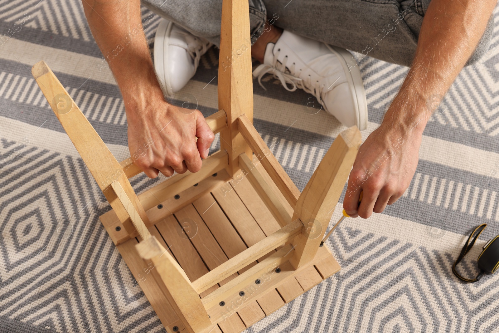 Photo of Man repairing wooden stool with screwdriver indoors, closeup