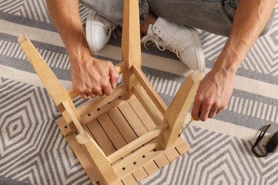 Photo of Man repairing wooden stool with screwdriver indoors, closeup