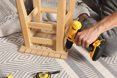 Photo of Man repairing wooden stool with electric screwdriver indoors, closeup