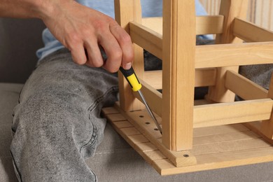 Man repairing wooden stool with screwdriver indoors, closeup